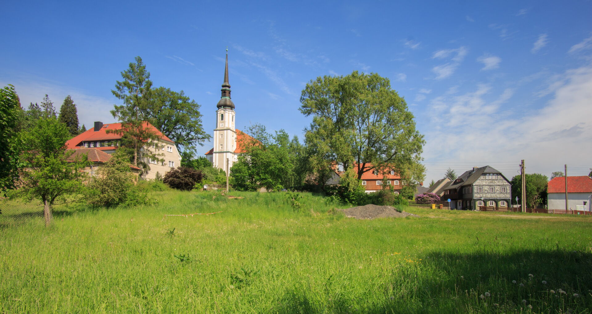 Ausblich auf die Kirche Cunewalde umgeben von Bäumen und Wiese im Vordergrund